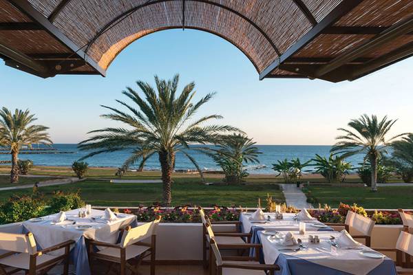 Außenterrasse des Athena Royal Beach Hotel mit Blick auf das Meer und Palmen.