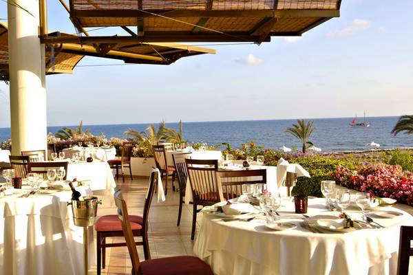 Außenbereich des Athena Royal Beach Hotels mit Tisch und Stühlen, Blick auf das Meer.