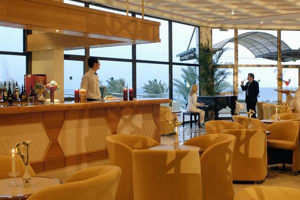 Bar im Athena Royal Beach Hotel mit Panoramafenstern und Blick auf das Meer.