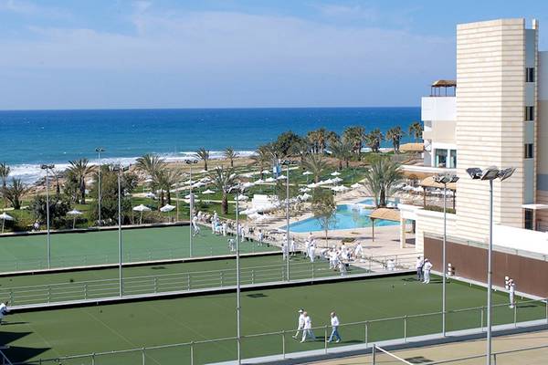 Aerial view of the Athena Royal Beach Hotel with outdoor tennis courts and a swimming pool by the ocean.