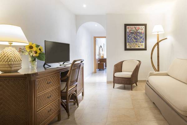 Innenansicht eines Zimmers im Princess Inspire Tenerife Hotel mit Schreibtisch, Sessel, Couch und Kunstwerk.