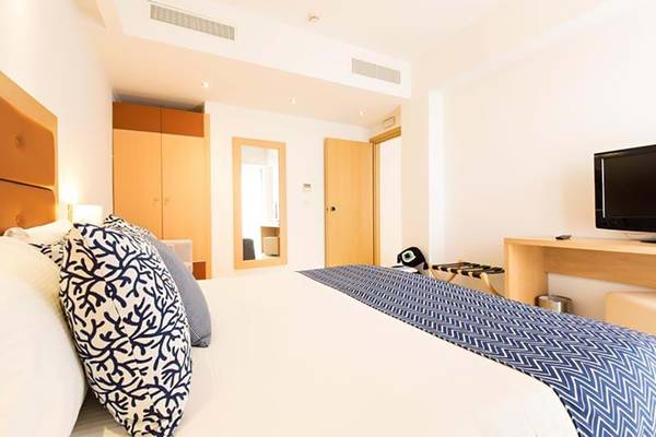 Schlafzimmer im Royal Blue Resort mit weißem Bett, blauen Kissen und Fernseher.