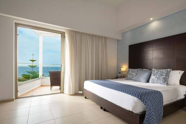 Hotelzimmer im Royal Blue Resort mit Balkon und Meerblick, Bett und Sessel draußen.