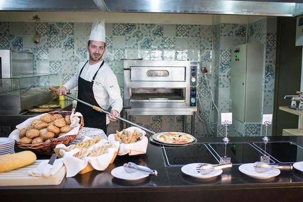 Koch im Royal Blue Resort mit einer Pizza und verschiedenen Gerichten in der Küche