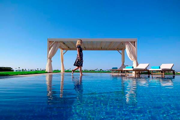Frau barfuß am Pool des Royal Blue Resorts, Sonnenschirm und Loungestühle im Hintergrund