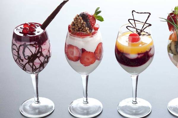 Vier fruchtige Cocktails in Gläsern mit Dekorationen wie Früchten und Schokoröllchen.