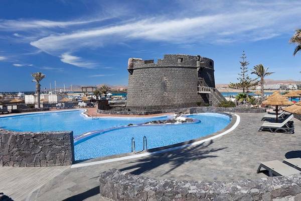Poolbereich des Barcelo Fuerteventura Castillo Hotels mit Blick auf eine alte Burg.