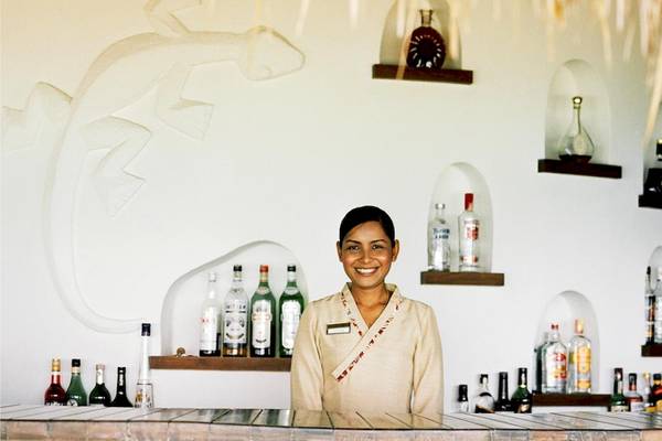 Rezeptionistin des Rayavadee Hotels steht lächelnd vor einer Bar mit vielen Flaschen.
