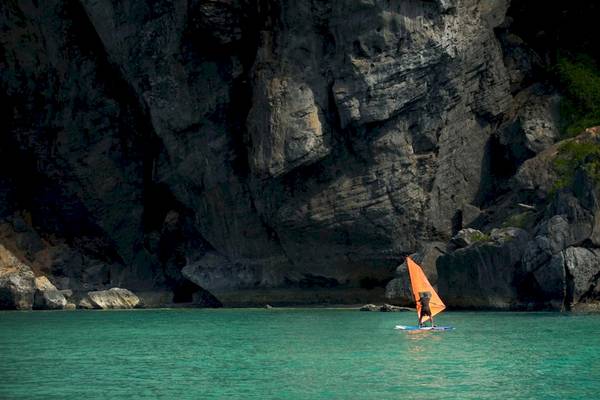Windsurfer segelt vor einer hohen Felswand