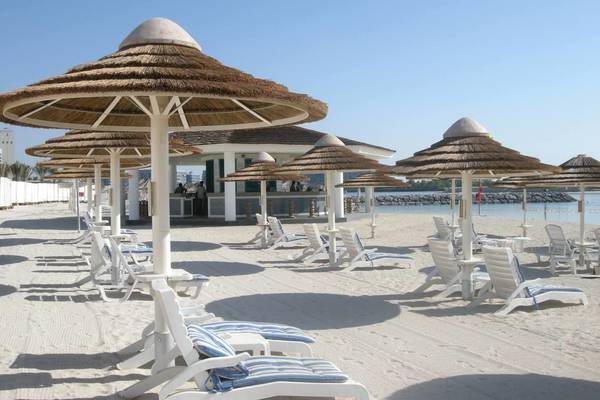 Strandszene mit weißen Sonnenliegen und Strohschirmen im Intercontinental Abu Dhabi