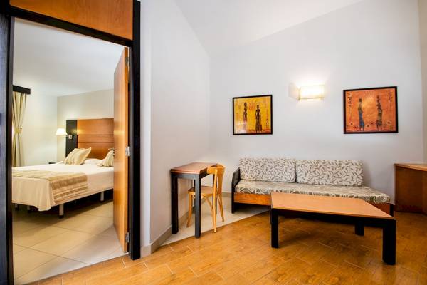 Innenansicht eines Zimmers im HL Miraflor Suites Hotel mit Bett, Tisch und Sofa.