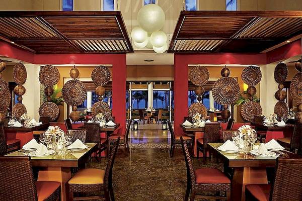 Innenansicht eines Restaurants im Secrets Royal Beach Punta Cana Hotel mit roten Säulen und Tischdekoration.
