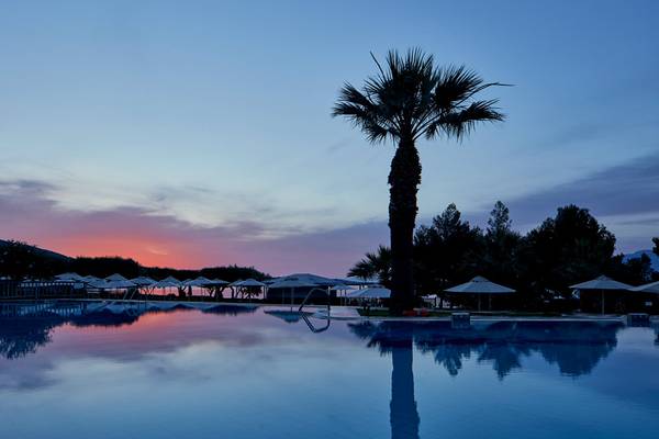 Abendstimmung am Pool im Candia Park Village mit Palme und Sonnenuntergang im Hintergrund.