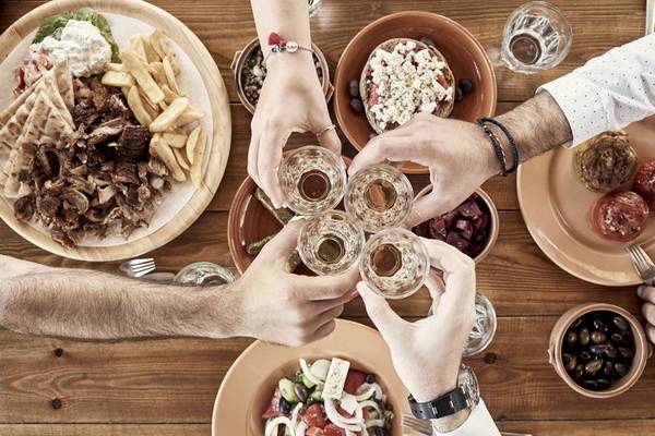 Menschen trinken auf griechisches Essen an einem Holztisch anstoßen.