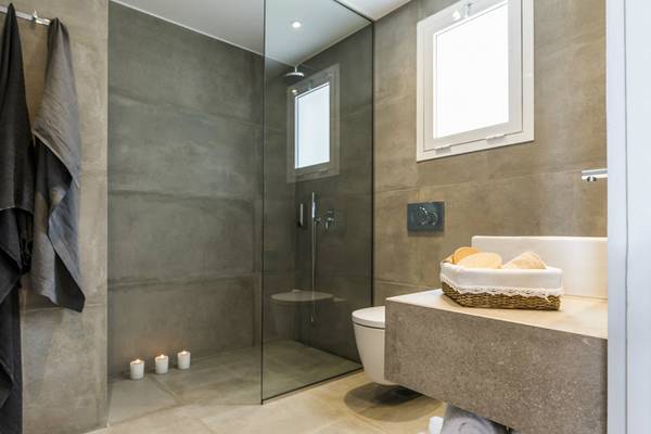 Badezimmer im Candia Park Village Hotel mit grauen Fliesen, Glasdusche und Waschbecken.