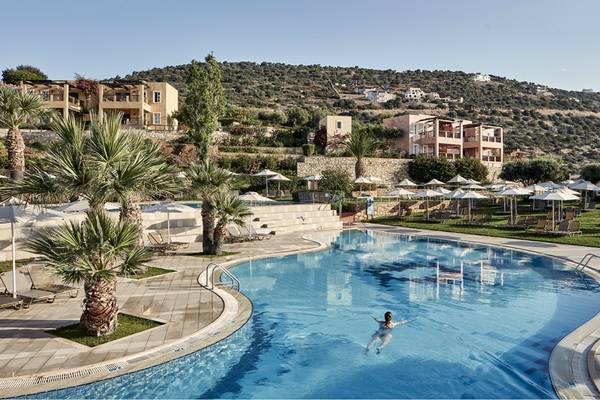 Person schwimmt im Pool des Candia Park Village Hotels, umgeben von Gebäuden und Landschaft.