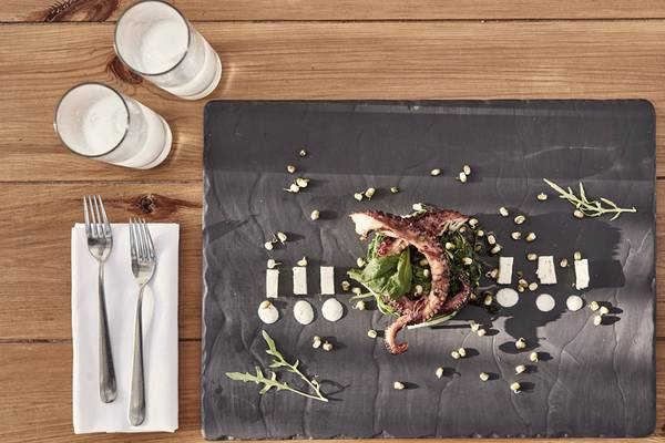 Candia Park Village Speisekarte Gericht mit Tintenfisch, Blattsalat und Beilagen auf einem schwarzen Teller.
