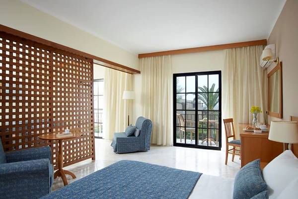 Innenansicht eines Zimmers im Porto Bello Beach Hotel mit Bett, Sofa, Tisch und Terrassentür.