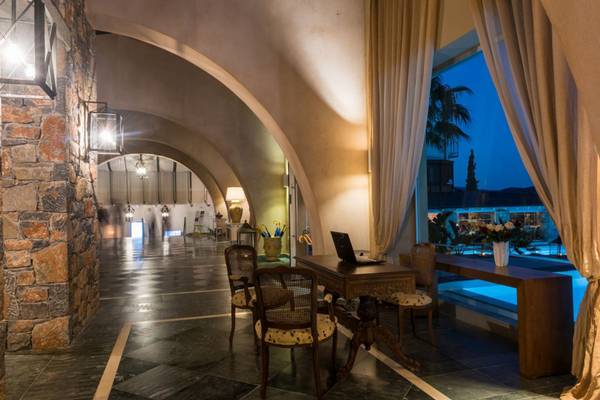 Innenansicht der Lobby im Elounda Village Resort & Spa mit Möbeln und Nachtansicht des Swimmingpools.