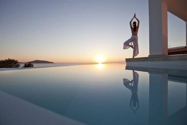 Eine Frau praktiziert Yoga an einem Pool bei Sonnenuntergang.