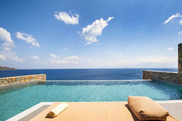Außenpool des Elounda Village Resort & Spa mit Blick auf das Meer und steinerne Einfassung.