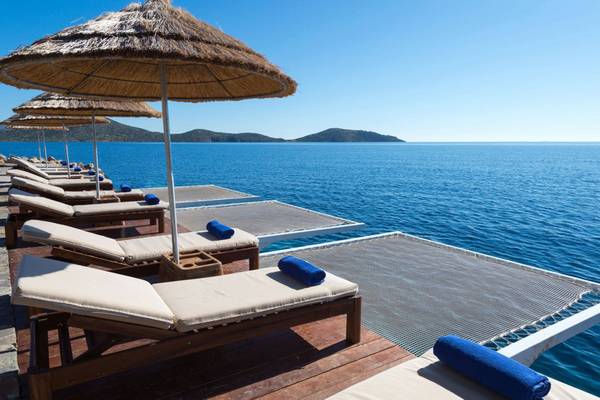 Elounda Village Resort & Spa: Liegestühle am Wasser mit Strohschirmen.