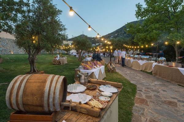 Abendessen im Freien im Elounda Village Resort & Spa mit langen Tischen und Bäumen.