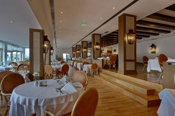 Innenansicht des Restaurants im Elounda Village Resort & Spa mit gedeckten Tischen und Holzböden.