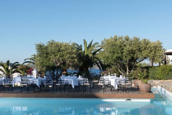 Außenbereich des Elounda Village Resorts mit Swimmingpool und bestuhlten Tischen.