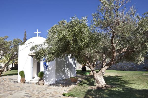 Außenansicht der Kapelle des Elounda Village Resort & Spa, umgeben von Bäumen und Pflanzen.