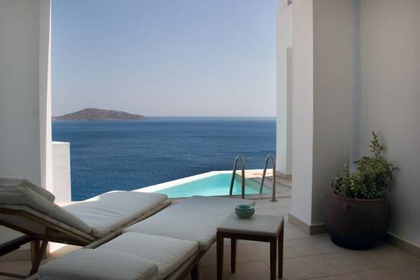 Terrasse mit Meerblick im Elounda Village Resort & Spa mit weißen Liegen, einem kleinen Tisch und einem Topf mit Pflanzen.