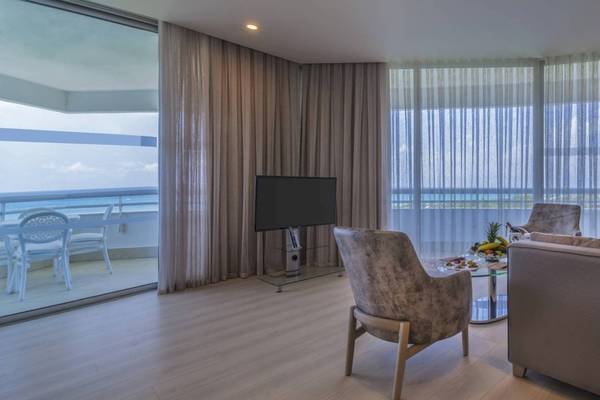 Wohnzimmer im Concorde De Luxe Resort mit Meerblick, Fernseher, Tisch, Stühlen und Balkonmöbeln.