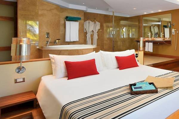 Ein luxuriöses Zimmer im Shandrani Beachcomber Resort & Spa mit einem großen Bett, roten Kissen, einem Fernseher, einem Badezimmer mit Badewanne und einer Holzeinrichtung.
