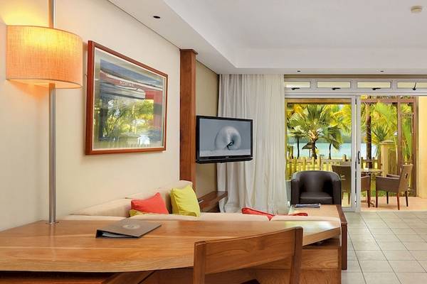 Innenansicht einer Suite im Shandrani Beachcomber Resort & Spa mit einem Bett, einem Fernseher, einem Schreibtisch und einem Balkon.