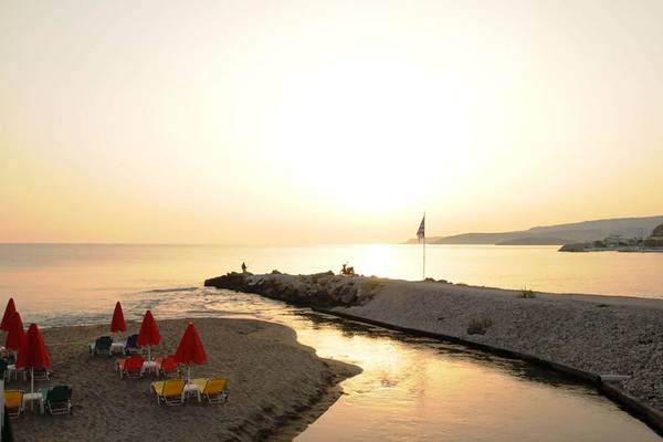 Sonnenuntergang am Strand des Kalyves Beach Hotels mit Liegestühlen und roten Sonnenschirmen.