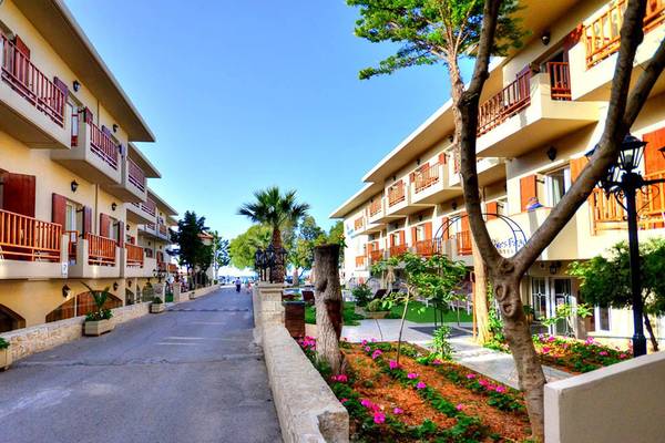 Die Allee des Kalyves Beach Hotels mit gepflegten Gärten und hohen Gebäuden.