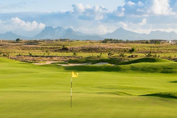 Golfplatz mit Wasserhindernis und Bergen im Hintergrund, Golfspieler und Golfwagen.