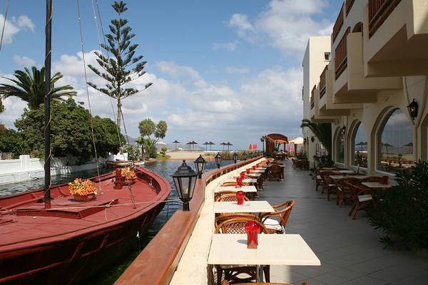 Terrasse des Kalyves Beach Hotels mit einem roten Boot im Kanal