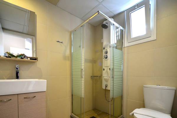 Badezimmer im Kalyves Beach Hotel mit Glasdusche, Waschbecken und Toilette.