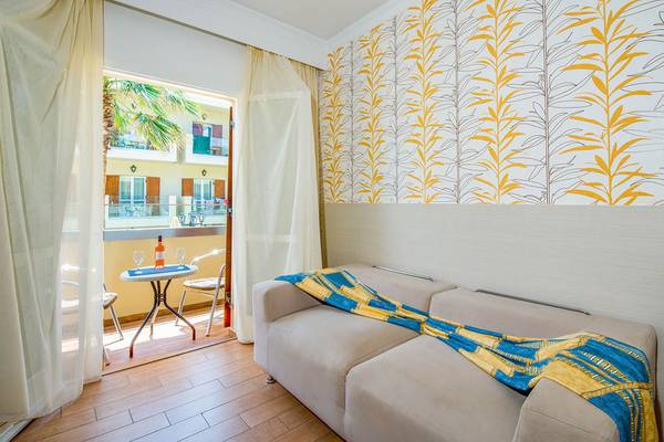 Zimmer im Kalyves Beach Hotel mit Balkon, Sofa, Tisch und Blick auf die Straße.