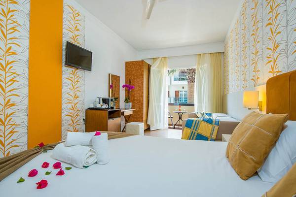Innenansicht eines Zimmers im Kalyves Beach Hotel mit farbenfrohen Wänden, einem Bett, Fernseher und Balkon.