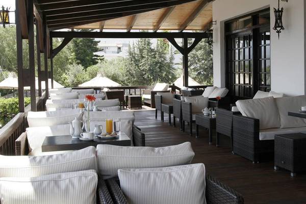 Terrasse des Hersonissos Maris Hotels mit vielen weißen Möbeln und Kissen, umgeben von Bäumen.