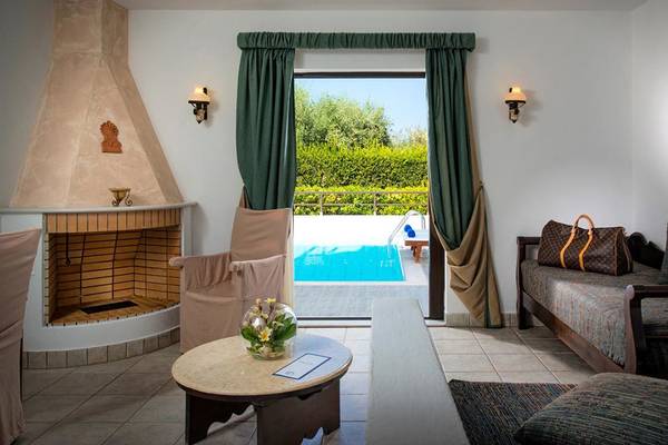 Innenansicht des Hersonissos Maris Hotels mit Wohnbereich, Kamin, Tisch, Sofa und Poolzugang.