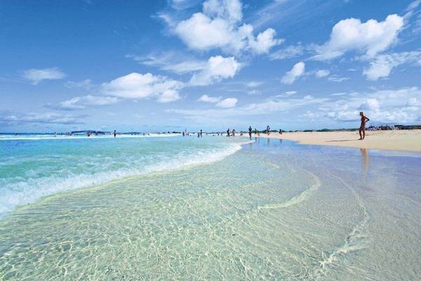 Strand mit kristallklarem Wasser und blauem Himmel, wo Menschen sich entspannen und schwimmen.