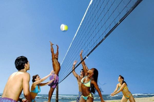 Gruppe von Männern und Frauen spielt Volleyball auf dem Strand im Freien.