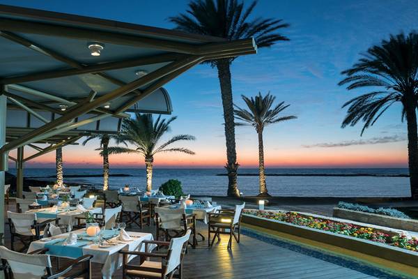 Außenterrasse des Pioneer Beach Hotels bei Sonnenuntergang mit Blick auf das Meer und Palmen.