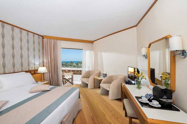 Innenansicht des Pioneer Beach Hotel Zimmers mit Meerblick, Bett, Sesseln und Schreibtisch.