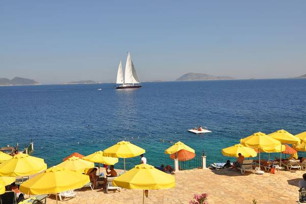 Ein Segelboot auf dem Meer vor einem Hotelstrand mit gelben Sonnenschirmen und Leuten.