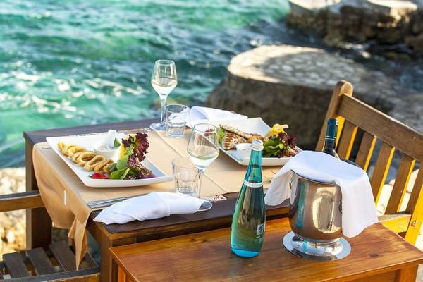 Tisch am Wasser im Cappari Hotels Aquarius mit Gerichten, Wein und Wasser.