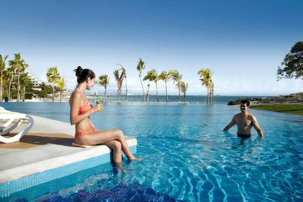 Eine Frau in einem roten Bikini sitzt am Rand des Pools und ein Mann steht im Wasser.